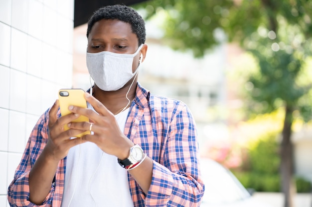 Homem usando uma máscara facial e usando seu telefone celular ao ar livre