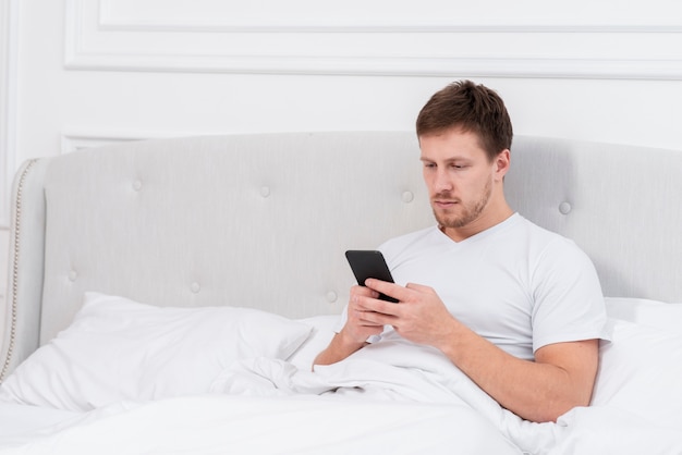Foto grátis homem verificando seu telefone depois de acordar com espaço de cópia