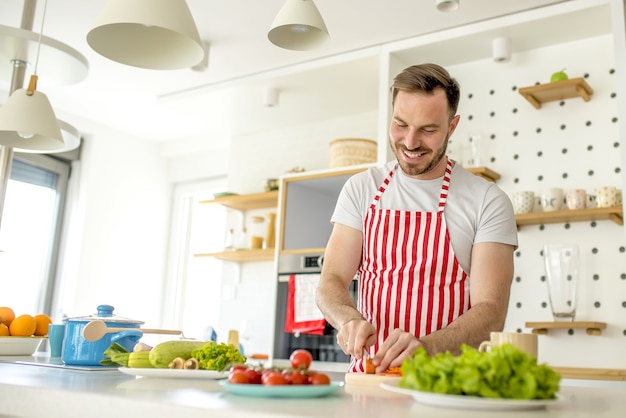 Homem vestindo um avental branco com linhas vermelhas e cozinhando algo na cozinha