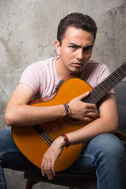 Homem vestindo uma camisa lisa na cadeira, segurando uma guitarra.