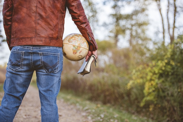 Homem vestindo uma jaqueta de couro e jeans segurando um globo de mesa e a bíblia