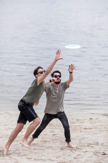 Homens adultos correndo na praia para pegar frisbee