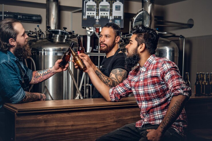 Foto grátis homens caucasianos, negros e indianos tatuados barbudos elegantes bebendo cerveja artesanal na microcervejaria.
