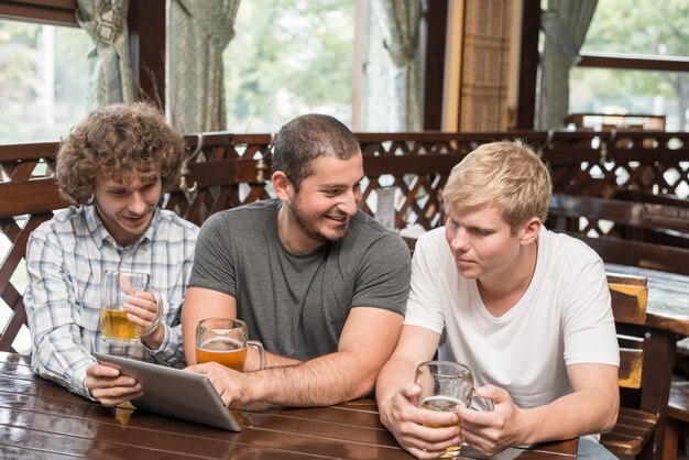 Homens com cerveja usando tablet e conversando no bar