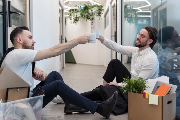 Homens de tiro completo tilintando copos no trabalho