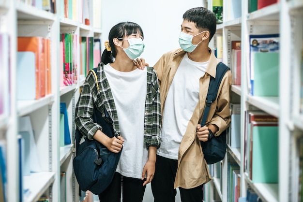 Homens e mulheres carregando uma mochila e procurando livros na biblioteca.