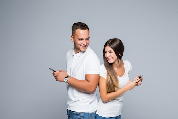 Homens e mulheres sorrindo, casal em pé com telefones celulares nas mãos, isolados em um fundo cinza