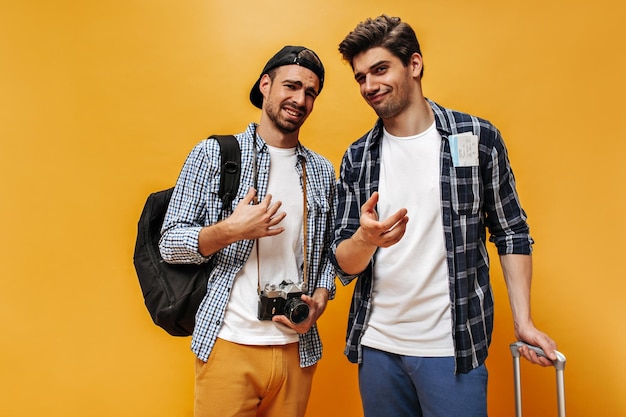 Homens insatisfeitos emocionais olham para a câmera em fundo laranja Jovens viajantes desapontados posam isolados