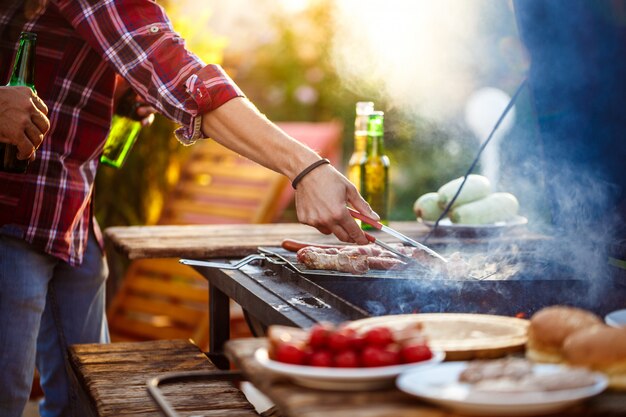 Homens jovens assar churrasco na grelha na zona rural de casa de campo.