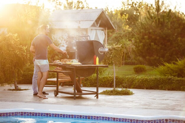 Homens jovens assar churrasco na grelha na zona rural de casa de campo.