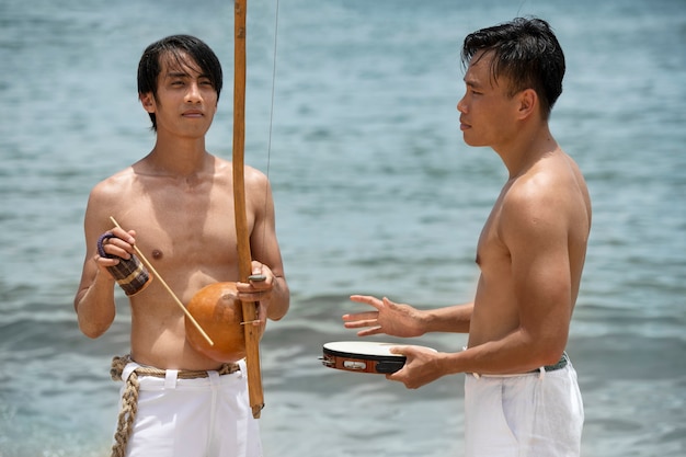 Homens na praia praticando capoeira junto com arcos de madeira