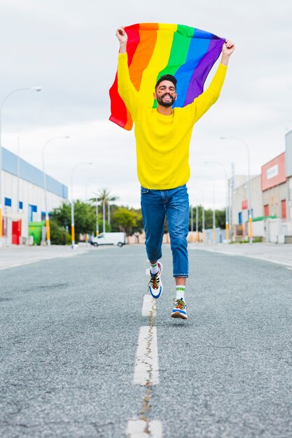 Homossexual correndo estrada segurando bandeira LGBT sobre a cabeça