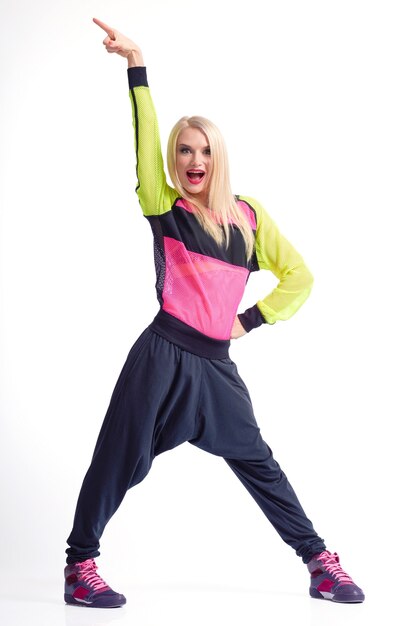 É hora de partir. Foto de estúdio de corpo inteiro vertical de uma alegre dançarina loira em roupas esportivas, gritando animadamente com o braço levantado no ar isolado