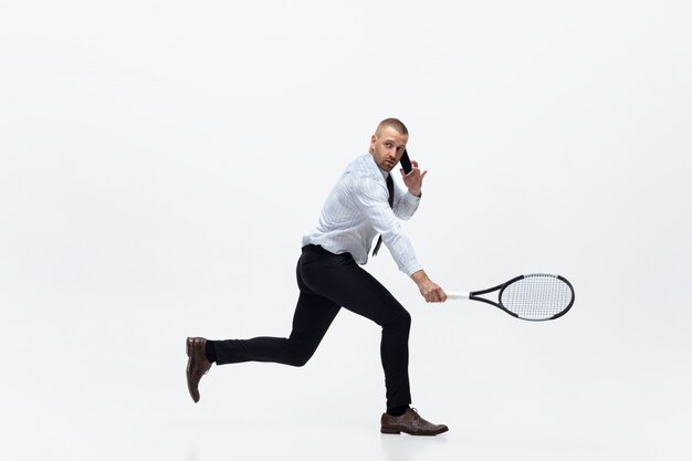 Hora do movimento. O homem na roupa do escritório joga o tênis isolado no branco. Empresário treinando em movimento, ação. Olhar incomum para desportista, nova atividade. Esporte, estilo de vida saudável.