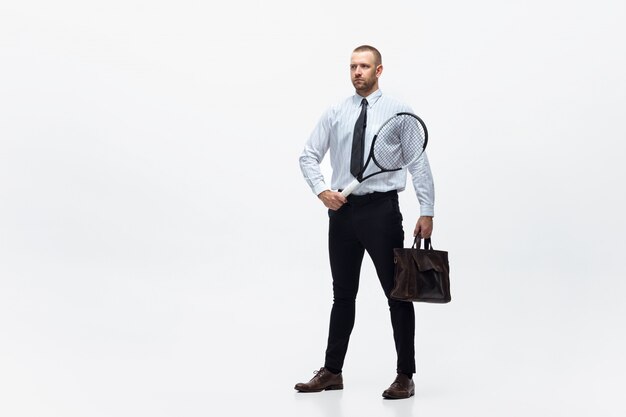 Hora do movimento. O homem na roupa do escritório joga o tênis isolado no branco. Empresário treinando em movimento, ação. Olhar incomum para desportista, nova atividade. Esporte, estilo de vida saudável.