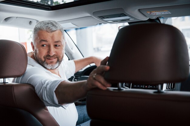 Humor alegre. Dirigindo um carro em marcha à ré. Olhando para trás. Homem em seu automóvel novo