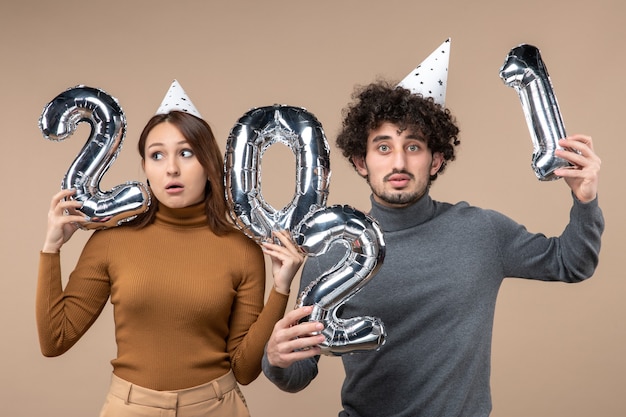 Humor de ano novo com jovem casal usando poses de chapéu de ano novo para a câmera garota mostrando ee cara com e em cinza