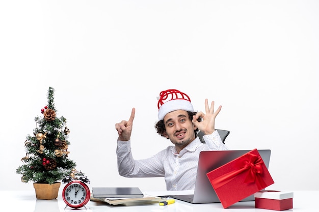 Humor de ano novo com jovem empresário animado e sorridente surpreso sentado no escritório e fazendo um gesto perfeito no fundo branco