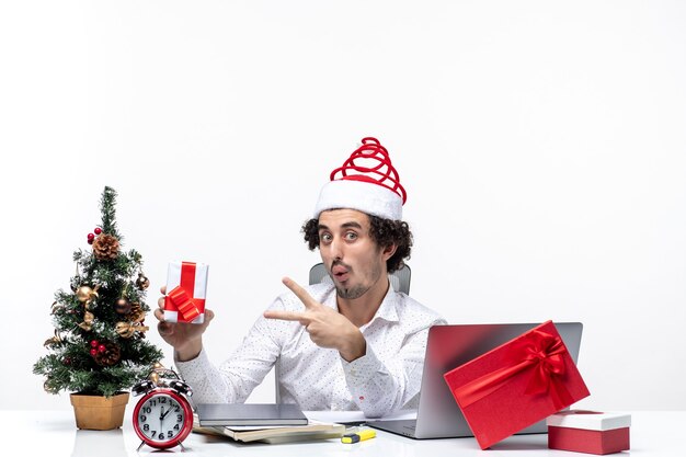 Humor de Natal com jovem empresário engraçado animado emocional com chapéu de Papai Noel e apontando seu presente no fundo branco