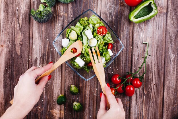 Idéias de almoço ou jantar. Mulher sacode a salada fresca de vegetação, abacate, pimenta verde