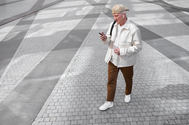Foto grátis idoso ao ar livre na cidade usando smartphone com fones de ouvido