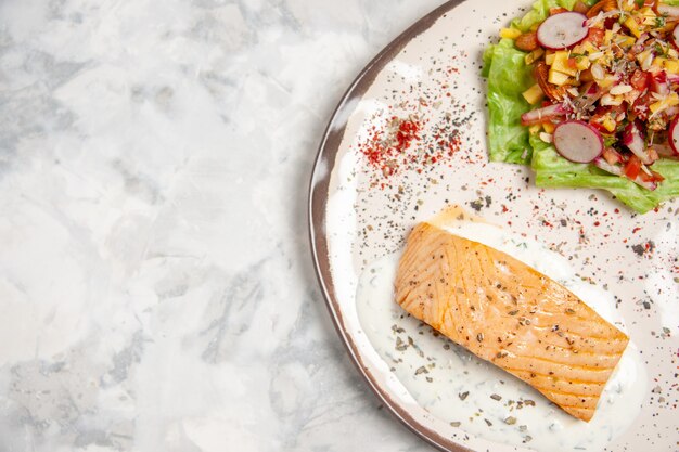 Imagem aproximada de farinha de peixe e salada deliciosa em um prato em uma superfície branca manchada com espaço livre