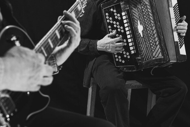 Imagem aproximada de mãos masculinas tocando violão e acordeão Fotografia em preto e branco Cultura retrô