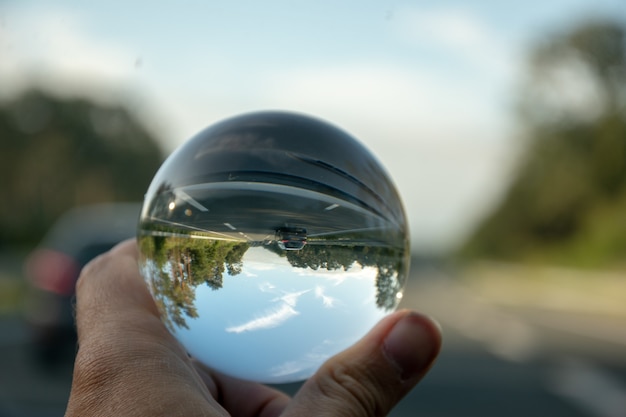 Imagem aproximada de uma pessoa segurando uma bola de cristal com o reflexo das árvores