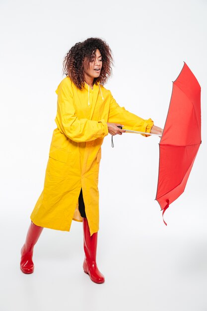 Imagem completa da jovem mulher africana na capa de chuva, abrindo o guarda-chuva