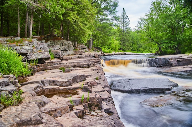 Imagem da cachoeira criando um pequeno desfiladeiro com camadas de rochas cinzentas na floresta