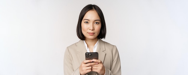Imagem da empresária asiática de terno segurando o celular usando o aplicativo de smartphone sorrindo para a câmera whi