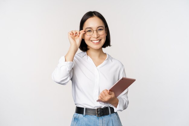 Imagem da jovem empresária asiática empresária em óculos segurando tablet e parecendo profissional em óculos fundo branco