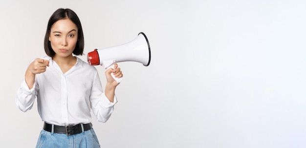 Imagem da mulher asiática moderna com megafone apontando para você câmera fazendo anúncio fundo branco