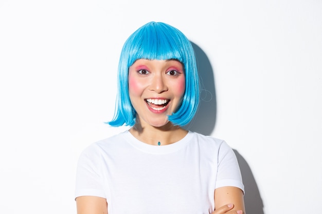 Imagem de animada linda garota asiática com fantasia de halloween e peruca azul, sorrindo divertido, em pé.