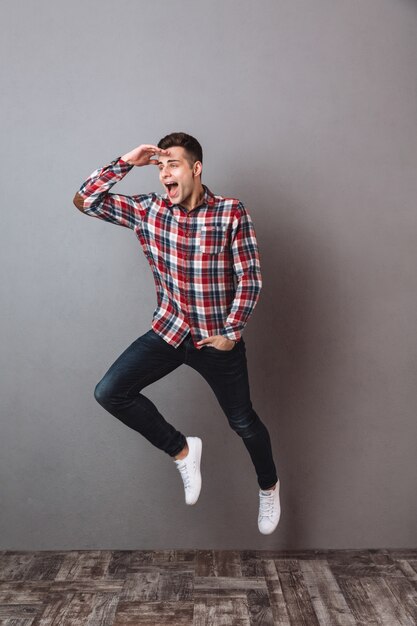 Imagem de corpo inteiro de homem feliz em jeans e camisa, jimping e desviar o olhar com o braço no bolso