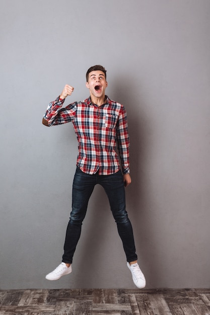 Imagem de corpo inteiro de homem gritando de camisa e calça jeans pulando e olhando para cima