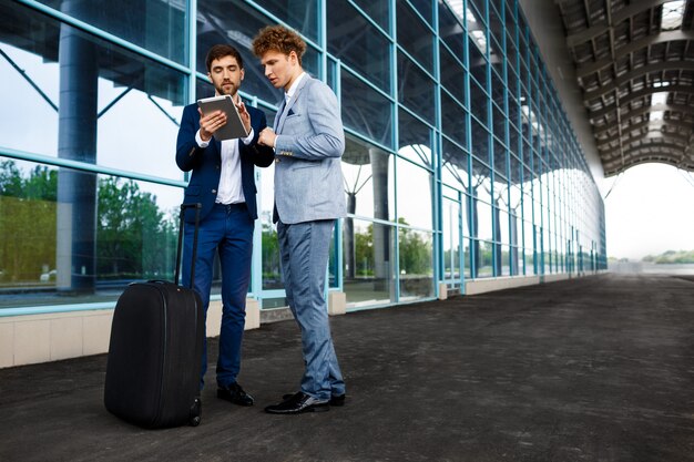 Imagem de dois jovens empresários falando na estação e segurando o tablet