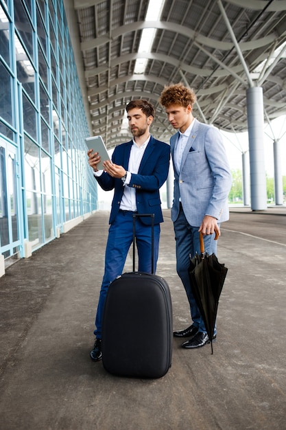 Imagem de dois jovens empresários falando no terminal e segurando o tablet