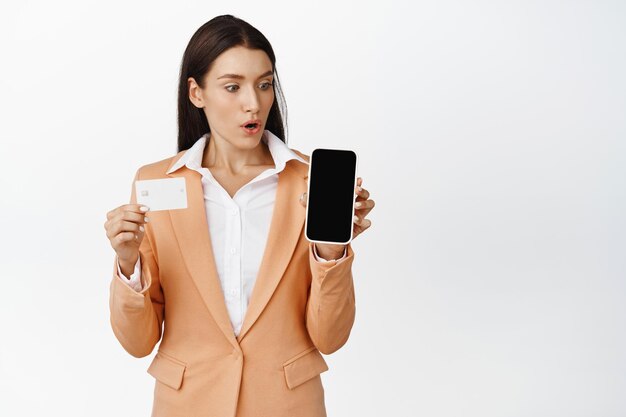 Imagem de empresária olhando espantada com o celular mostrando a tela e o cartão de crédito Conceito de finanças e pagamento on-line