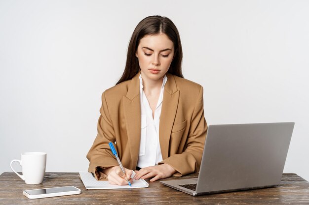 Imagem de empresária trabalhando no escritório sentado à mesa com laptop escrevendo documentos posando em fo...