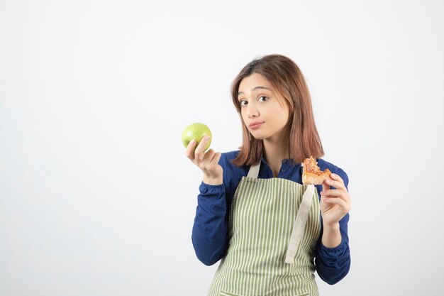 Imagem de jovem cozinheiro escolhendo o que comer pizza e maçã verde.