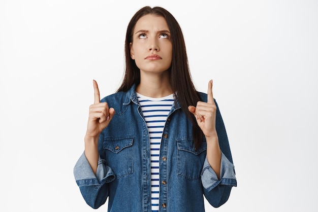 Foto grátis imagem de jovem séria e sombria reclama apontando e olhando para cima com condenação e julgamento não gosta de smth má posição contra fundo branco opinião negativa