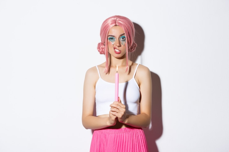 Foto grátis imagem de menina irritada na peruca rosa, segurando uma vela e mostrando os dentes, comemorando o dia das bruxas, em pé sobre um fundo branco.