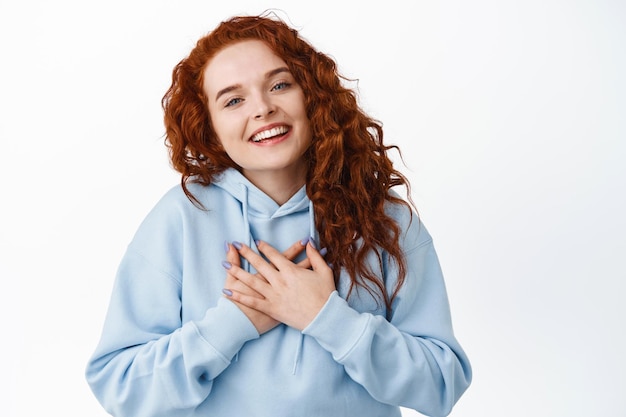 Imagem de menina ruiva emocionada e lisonjeada recebendo prácas, de mãos dadas no peito e dizer obrigado, sorrindo agradecida no branco