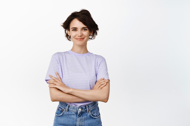 Imagem de modelo feminino morena confiante, garota parece assertiva e pronta, cruze os braços no peito como profissional, sorrindo rosto presunçoso, de pé sobre fundo branco