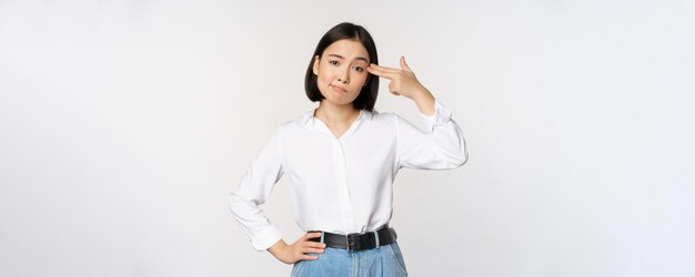 Imagem de mulher asiática cansada irritada por smth apontando dedos para a cabeça dela em pé sobre fundo branco copiar espaço