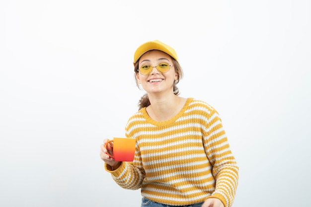 Imagem de mulher jovem e bonita de óculos em pé e segurando uma caneca. foto de alta qualidade