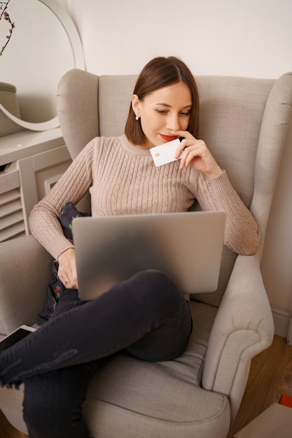 Imagem de mulher simpática e satisfeita segurando um cartão de crédito com espaço de cópia usando um laptop