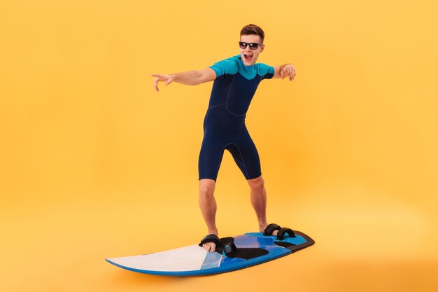 Imagem de surfista feliz em roupa de mergulho e óculos de sol usando prancha como na onda