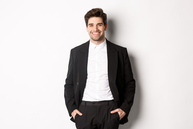 Imagem de um homem bonito, caucasiano, em traje de festa, sorrindo satisfeito, participando de um evento formal, em pé sobre um fundo branco